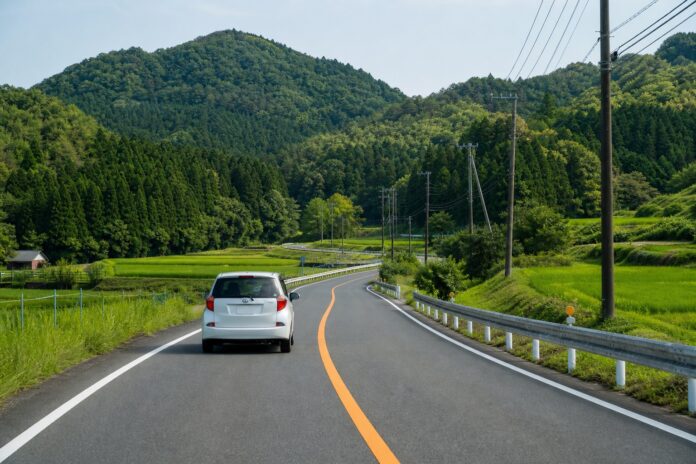 A rental car driving safely on the left side of a rural road in Japan
