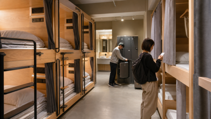 Travelers store luggage beside curtained capsule and hostel-style sleeping units in a clean Japanese shared accommodation