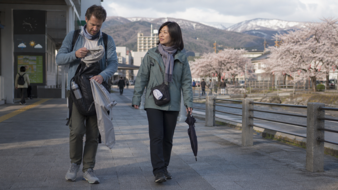 Travelers adjust breathable, warm and weatherproof clothing layers during a variable Japanese spring day with blossoms and distant snow
