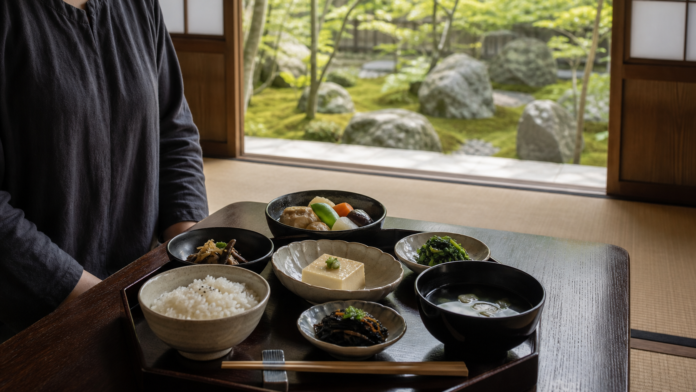 A plant-based shojin ryori tray with rice, soup, tofu, simmered vegetables, greens, mushrooms and seaweed in a quiet tatami room overlooking a temple garden