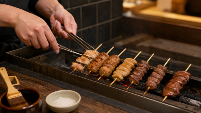 Yakitori cook rotating fully cooked chicken thigh, meatball, skin and organ skewers across separate charcoal heat zones