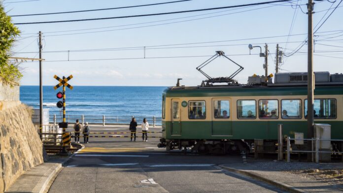 湘南の海を背景に鎌倉の海辺の踏切を通過する江ノ電風の電車